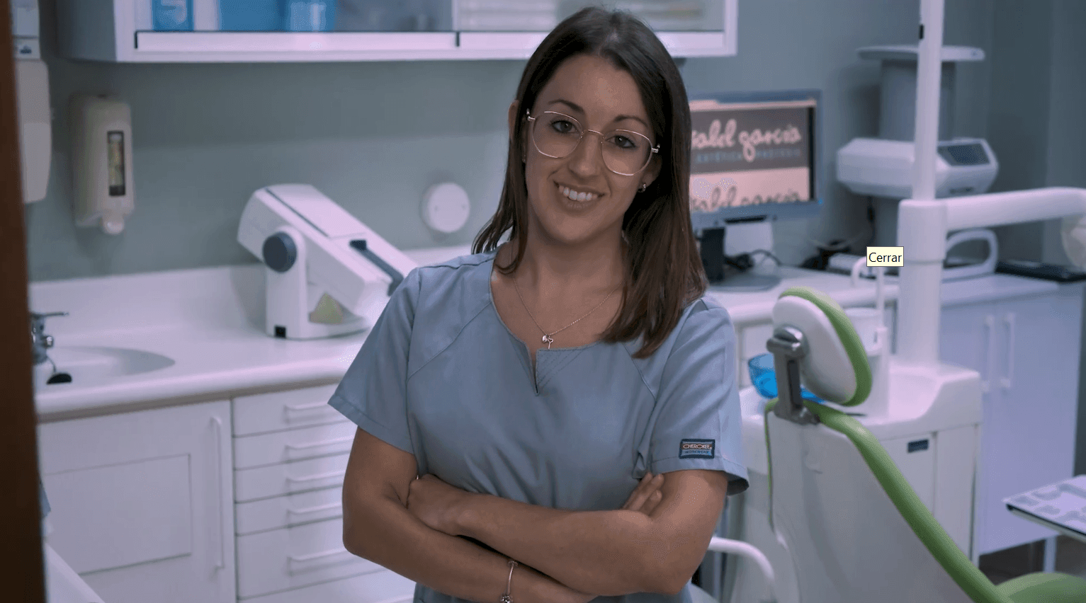 Smiling woman in dental scrubs standing in a modern dental office with equipment in the background.